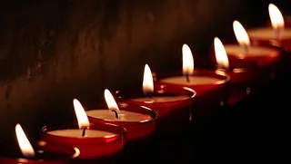 Mehrere brennende Teelichter in roten Gläsern stehen in einer Reihe und spenden warmes Licht in dunkler Umgebung.