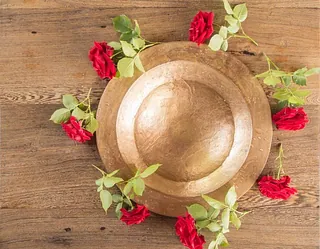 Zwei goldfarbene Teller liegen auf einem Holztisch, dekoriert mit roten Rosen und grünen Blättern.